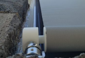Close-up image of the electric roller shade bracket installed on a textured stone wall, showing precision fit and robust hardware.