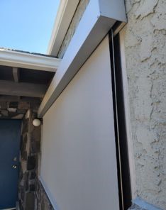 Side profile of motorized shades and housing on textured stucco wall, showing integration of electric window shades and guide channels.